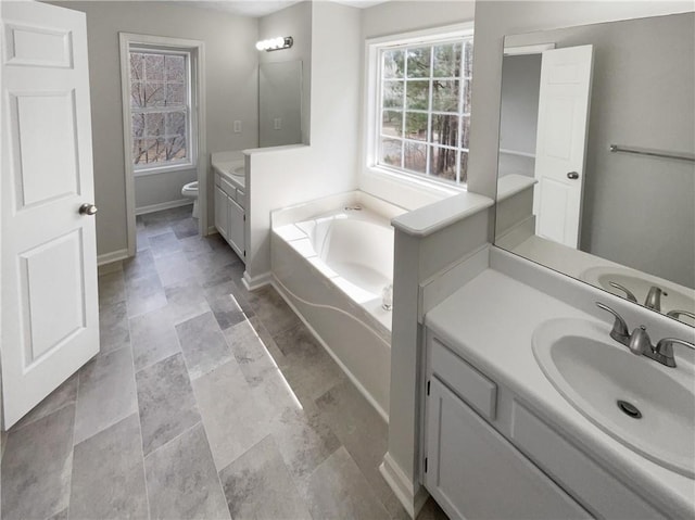 full bathroom with a bath, baseboards, two vanities, a sink, and toilet