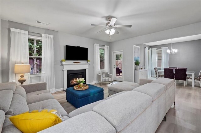 living room with light wood-type flooring and ceiling fan with notable chandelier