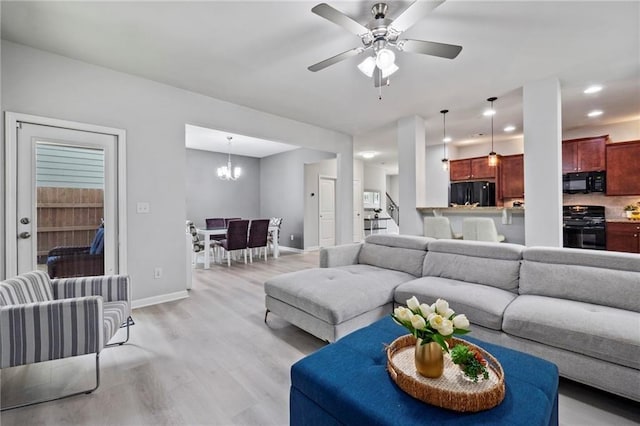 living room featuring ceiling fan with notable chandelier and light hardwood / wood-style floors