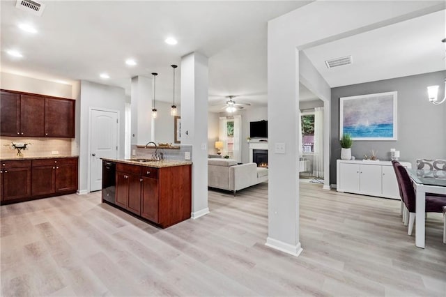 kitchen with pendant lighting, light stone counters, sink, ceiling fan, and light hardwood / wood-style floors