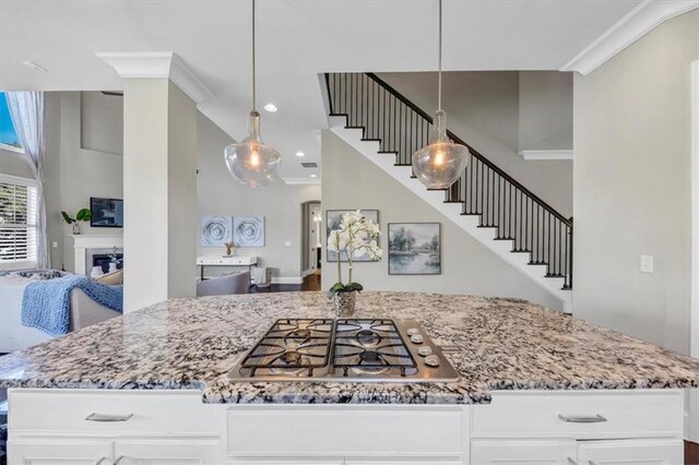 kitchen featuring stainless steel gas cooktop, a center island, hanging light fixtures, ornamental molding, and white cabinets