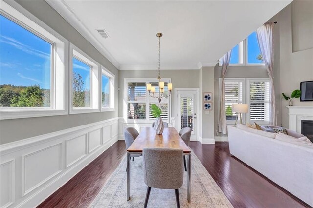 dining area with crown molding, dark wood-type flooring, a wealth of natural light, and a notable chandelier