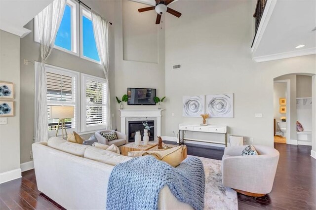 living room with dark wood-type flooring, ceiling fan, and a high ceiling