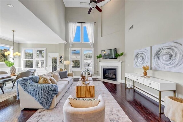 living room featuring dark wood-type flooring, a healthy amount of sunlight, ceiling fan with notable chandelier, and a high ceiling