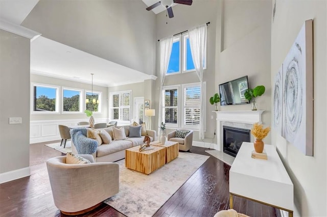 living room with dark wood-type flooring, ceiling fan, ornamental molding, and a fireplace