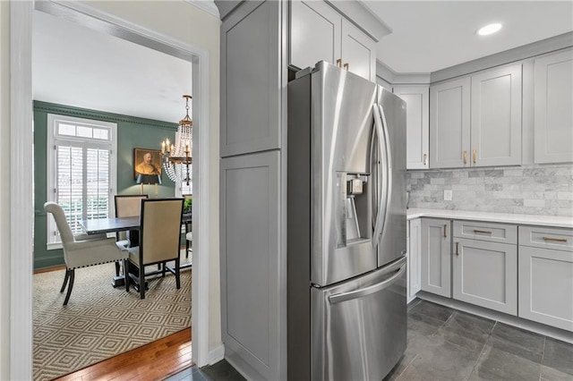 kitchen featuring gray cabinetry, crown molding, decorative backsplash, stainless steel refrigerator with ice dispenser, and an inviting chandelier