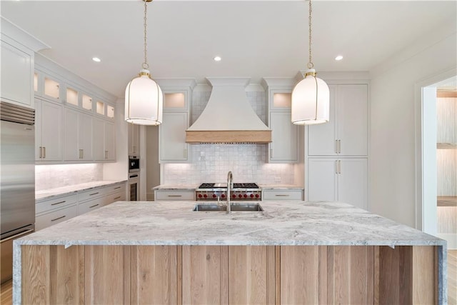 kitchen with premium range hood, white cabinets, hanging light fixtures, appliances with stainless steel finishes, and a large island