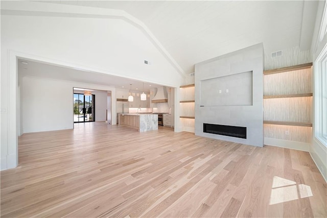 unfurnished living room featuring a large fireplace, light hardwood / wood-style floors, high vaulted ceiling, and sink