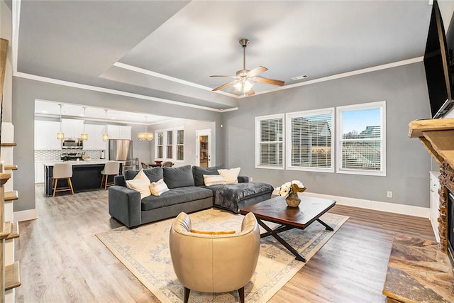 living room featuring a stone fireplace, ceiling fan, ornamental molding, and light wood-type flooring