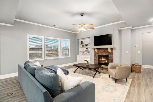 living room with ceiling fan, built in features, hardwood / wood-style floors, a fireplace, and ornamental molding