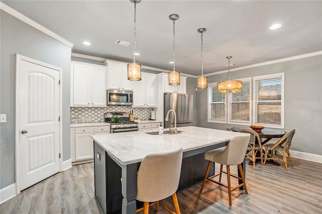 kitchen featuring a center island with sink, decorative light fixtures, white cabinets, and appliances with stainless steel finishes