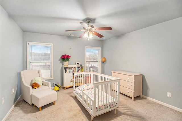 bedroom with ceiling fan, light colored carpet, and a crib