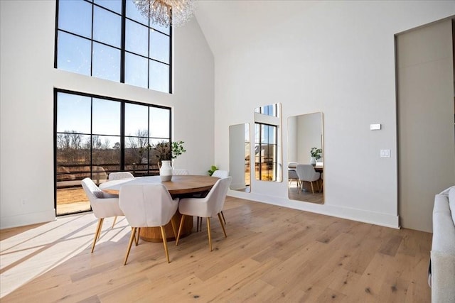 dining area with a towering ceiling, an inviting chandelier, and light wood-type flooring