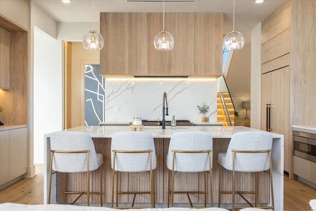 kitchen featuring decorative light fixtures, light brown cabinetry, and a breakfast bar area