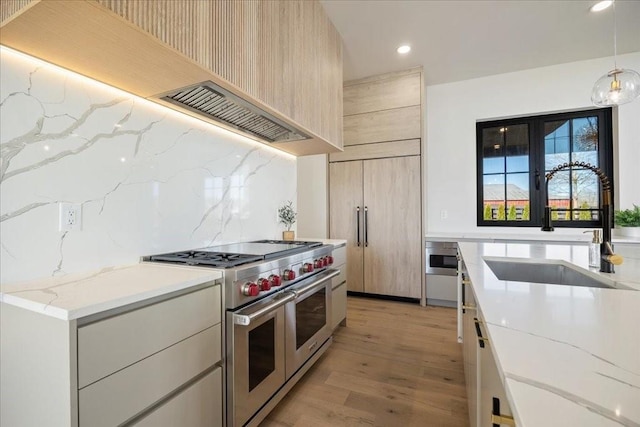 kitchen with sink, light brown cabinets, pendant lighting, light stone countertops, and range with two ovens