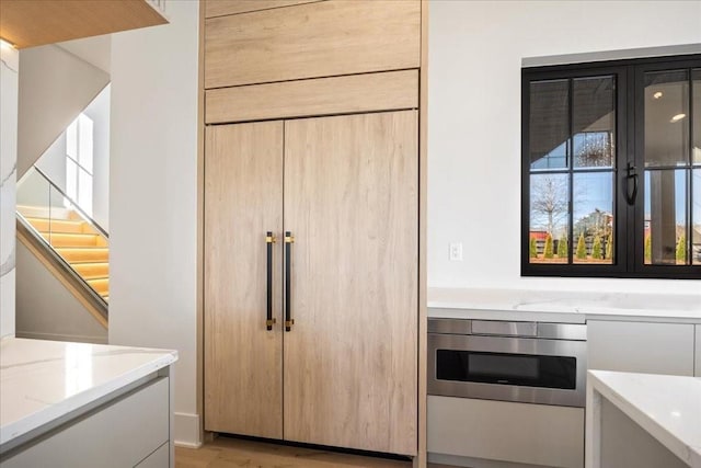 kitchen with light stone counters, light hardwood / wood-style flooring, oven, and light brown cabinets