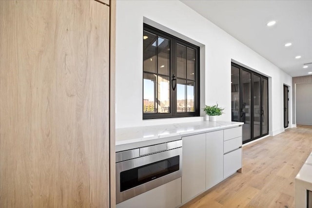 kitchen with white cabinetry, stainless steel microwave, light stone counters, and light hardwood / wood-style floors