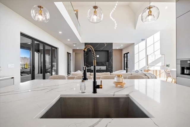 kitchen featuring light stone counters, a high end fireplace, sink, and hanging light fixtures