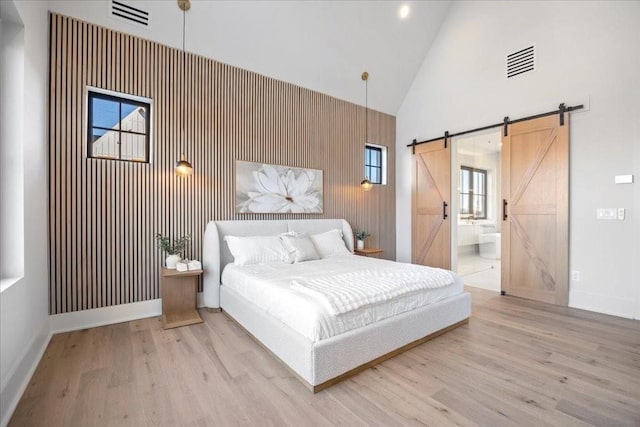 bedroom featuring ensuite bathroom, a barn door, high vaulted ceiling, and light hardwood / wood-style floors