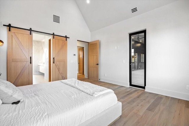 bedroom featuring a barn door, ensuite bath, high vaulted ceiling, and light hardwood / wood-style flooring