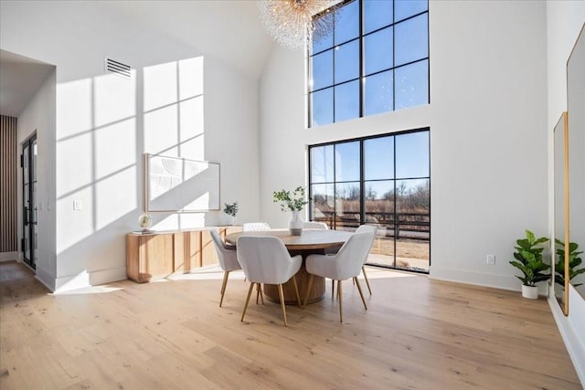 dining area with light hardwood / wood-style floors, a chandelier, and a high ceiling