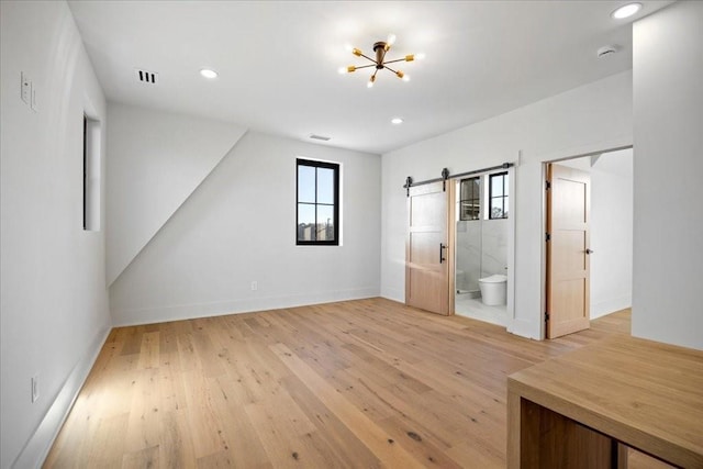 interior space with ensuite bathroom, a barn door, a chandelier, and light hardwood / wood-style flooring