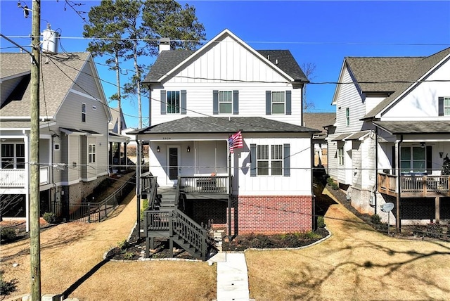 view of front facade featuring covered porch, brick siding, stairs, roof with shingles, and board and batten siding