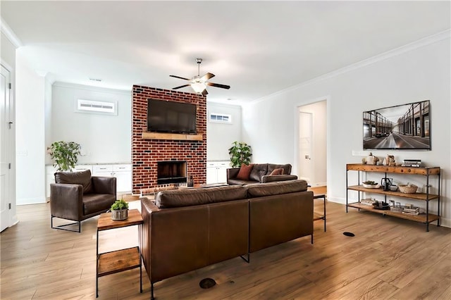 living room featuring a brick fireplace, ceiling fan, ornamental molding, and light wood-type flooring