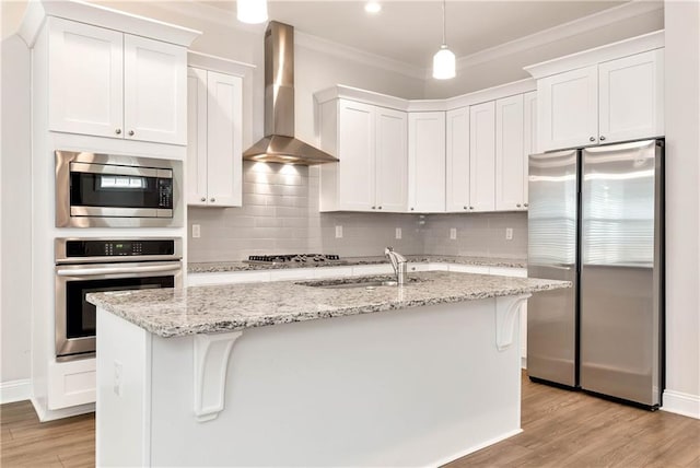 kitchen featuring stainless steel appliances, white cabinetry, a center island with sink, and wall chimney range hood