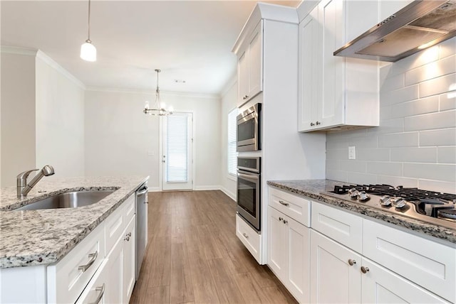 kitchen with sink, wall chimney exhaust hood, stainless steel appliances, hanging light fixtures, and white cabinets