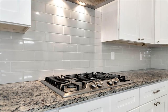 interior details with light stone countertops, stainless steel gas cooktop, white cabinetry, range hood, and tasteful backsplash