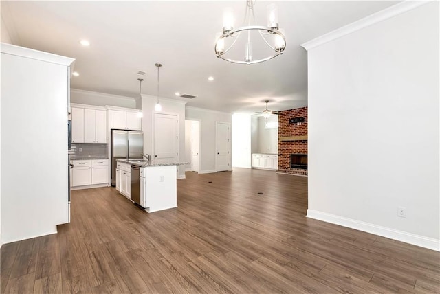 kitchen featuring stainless steel appliances, pendant lighting, a fireplace, white cabinetry, and an island with sink