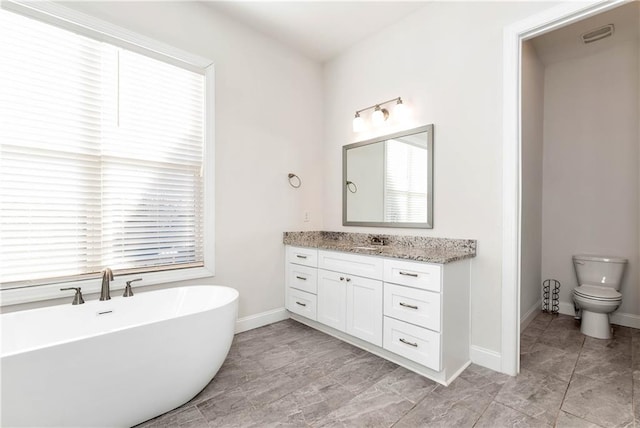 bathroom with toilet, a freestanding tub, vanity, and baseboards