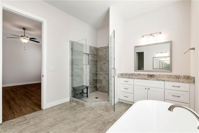 full bath featuring a stall shower, baseboards, a ceiling fan, a freestanding bath, and vanity