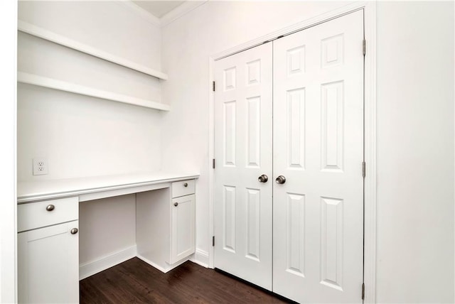 unfurnished office featuring dark hardwood / wood-style flooring, built in desk, and ornamental molding