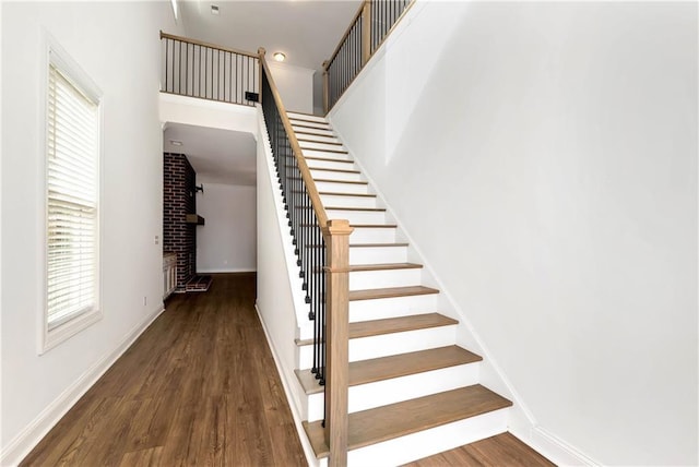 staircase featuring baseboards, a high ceiling, wood finished floors, and a healthy amount of sunlight