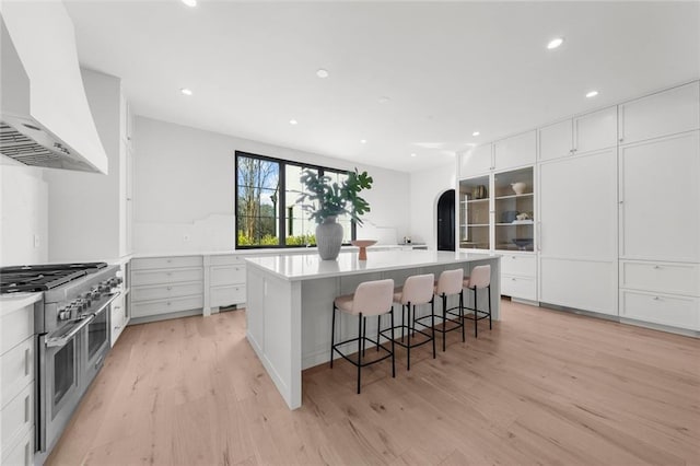 kitchen featuring white cabinetry, a large island, ventilation hood, range with two ovens, and a kitchen breakfast bar