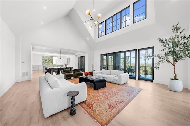 living room featuring an inviting chandelier, a wealth of natural light, light hardwood / wood-style flooring, and a high ceiling