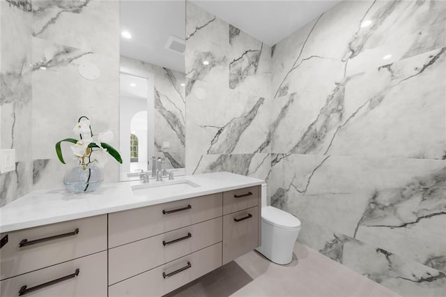 bathroom featuring toilet, tile walls, and vanity