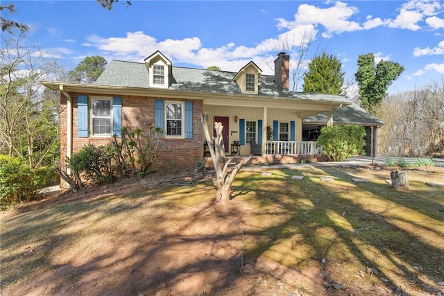 view of front of house with a porch, a chimney, a front yard, and brick siding