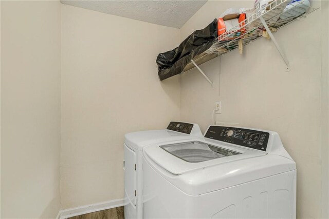 clothes washing area with washing machine and dryer, wood-type flooring, and a textured ceiling