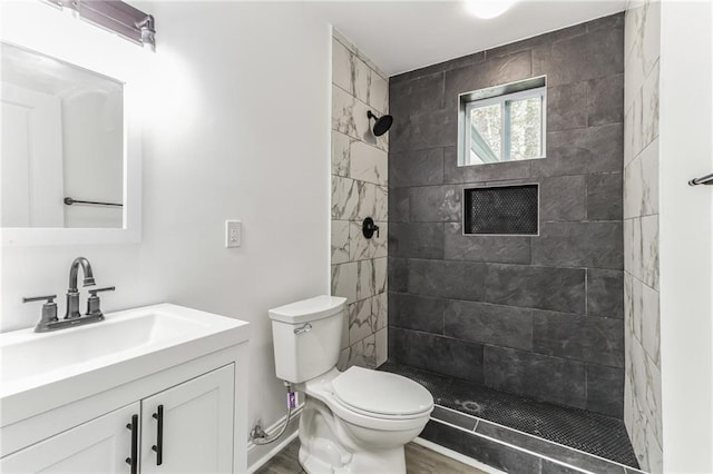 bathroom featuring a tile shower, hardwood / wood-style flooring, vanity, and toilet