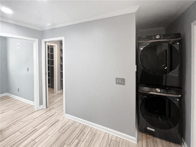 clothes washing area with crown molding, stacked washer / dryer, light wood-type flooring, baseboards, and laundry area