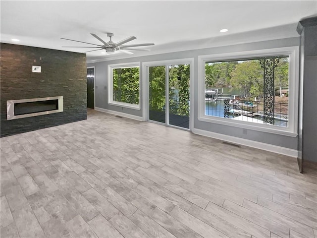 unfurnished living room with a ceiling fan, wood finished floors, a fireplace, baseboards, and visible vents