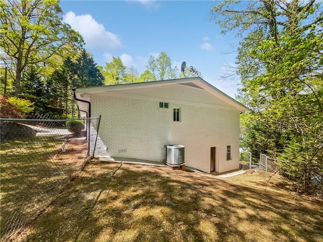 view of side of home with central AC unit, brick siding, and fence
