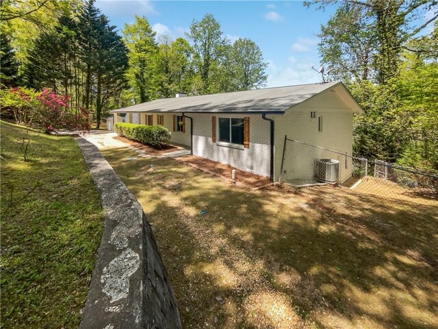 view of side of property featuring fence, brick siding, and central AC unit