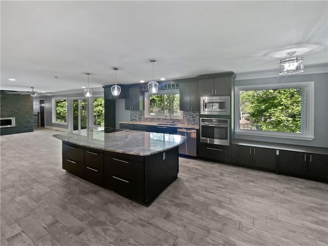 kitchen with stainless steel appliances, backsplash, a ceiling fan, a sink, and a center island