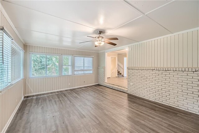 unfurnished living room with wooden walls, hardwood / wood-style floors, ceiling fan, and brick wall