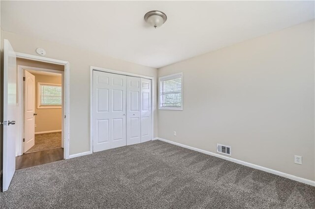 unfurnished bedroom with dark carpet, a closet, and multiple windows