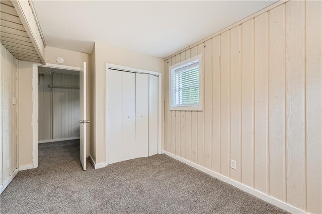 unfurnished bedroom with carpet floors, wooden walls, and a closet